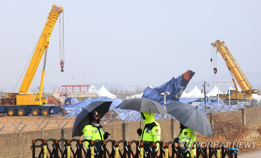 비 내리는 무안국제공항 (무안=연합뉴스) 김도훈 기자 = 5일 오전 우산을 쓰고 근무하는 경찰관들 뒤로 전남 무안국제공항 사고현장 및 꼬리 날개에 방수포가 덮여 있다. 2025.1.5 superdoo82@yna.co
