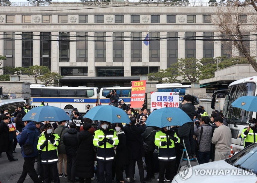 충돌 우려로 우산 펼쳐 든 경찰들 (서울=연합뉴스) 이진욱 기자 = 윤석열 대통령 탄핵심판 선고일 발표가 늦어지고 있는 가운데 20일 서울 종로구 헌법재판소 앞에서 경찰들이 탄핵 찬반 시위자들과 기자회견 참석자들 간