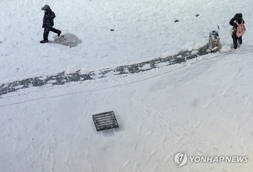 눈 위에 남겨진 고난의 흔적 (서울=연합뉴스) 김도훈 기자 = 서울 지역에 첫눈이자 폭설이 내린 4일 눈이 덮인 서울 종로구의 거리 위에 캐리어를 들고 이동하는 관광객 뒤로 흔적이 고스란히 남아 있다.2025.12