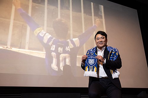 New Ulsan HD head coach Kim Hyun-seog poses with the team's scarf in front of a screen showing his p