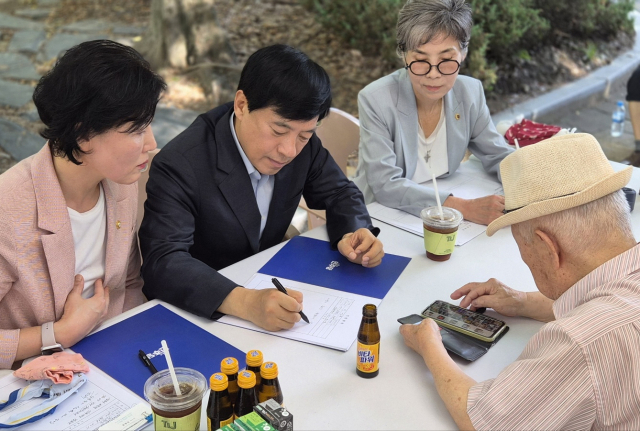 ▲30일 전주 서신길공원에서 열린 ‘이심전심 소통의 날’. 한 어르신이 딸의 훈장증 사진을 휴대폰으로 보여주며 불편함을 호소하자, 이성윤 의원(가운데)이 경청하며 메모하고 있다. ⓒ프레시안(양승수)