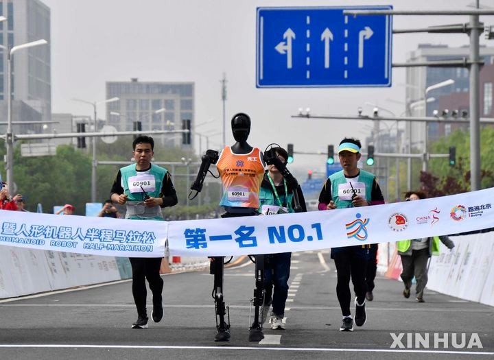 [베이징=신화/뉴시스] 19일 중국 베이징 이좡 경제기술개발구에서 열린 휴머노이드 로봇 하프마라톤에서 우승한 로봇 '톈궁 울트라'가 참가팀 인원들과 함께 달리고 있다.2025.04.20