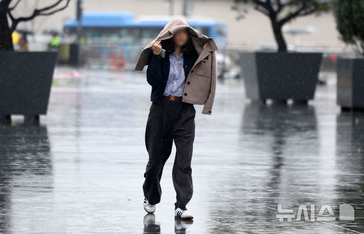 [서울=뉴시스] 김선웅 기자 = 수도권에 봄비가 내린 14일 서울 종로구 광화문광장에서 한 시민이 옷으로 비를 피하고 있다.2025.04.14.