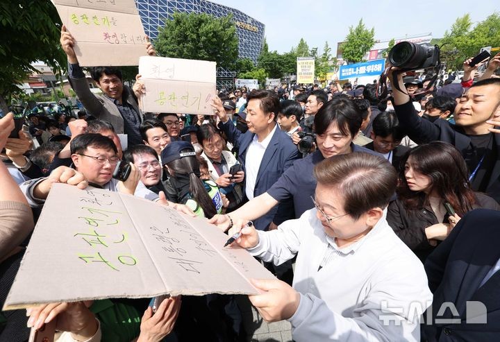 [전주=뉴시스] 조성봉 기자 = 민심을 청취하는 '경청 투어'에 나선 이재명 더불어민주당 대선후보가 7일 전북 전주시 완산구 풍남문 인근에서 공판연기를 환영하는 지지자의 응원 피켓에 사인을 해주고 있다.'공판연기 