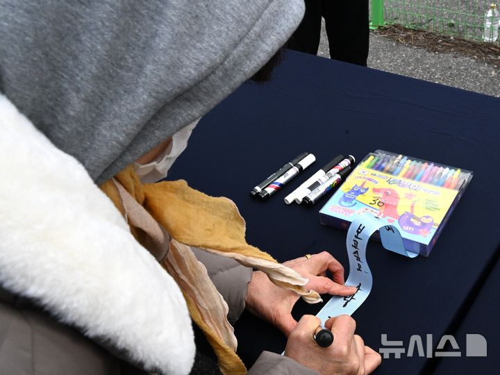 [무안=뉴시스] 이현행 기자 = 12·29 무안공항 제주항공 여객기 참사 유가족이 24일 오후 전남 무안군 무안국제공항에서 여객기 사고 현장 인근에 묶을 추모 리본에 글을 적고 있다.2025.12.24.lhh@n