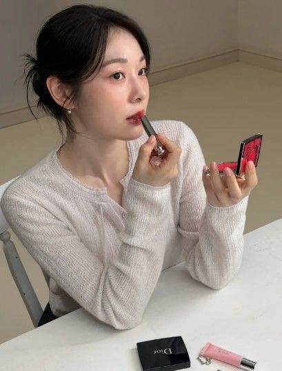 白いニットカーディガンを着たキム・ヨナが鏡を見ながら赤いリップを塗る