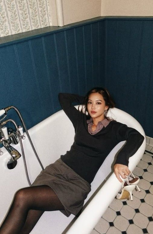 黒いニットとグレーのスカート姿で浴槽に腰掛け、白いハイヒールを手にするキム・ヒジョン