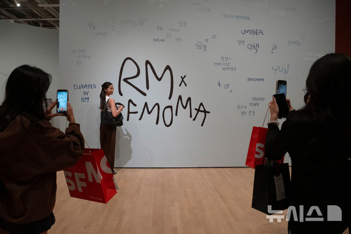 RMとSFMOMAの文字が書かれた展示室の壁を、来場者が撮影する