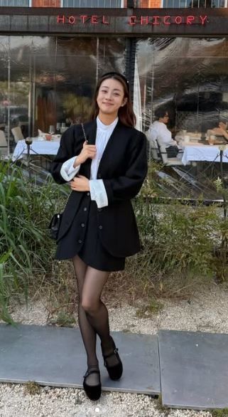 屋外で黒いジャケットと白いブラウス姿のカン・ソラが笑顔を見せている。