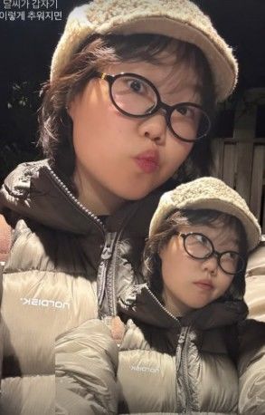 ベージュのファー帽子と眼鏡、ダウンジャケットを身につけ、鏡越しにセルフィーを撮るイ・スヒョン