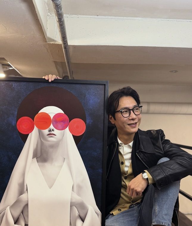 コ・ジヨンが、赤い円形のモチーフを配した作品の隣で笑顔を見せる