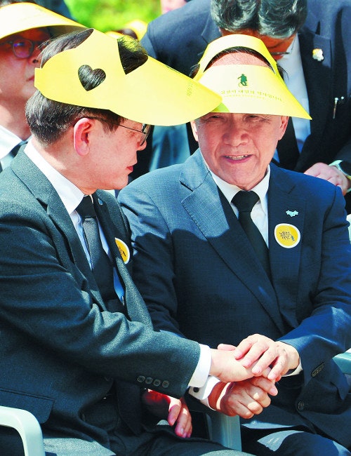 Hwang Woo-yea (right), the acting emergency response chief of the People Power Party, and Lee Jae-myung, the Democratic Party's leader, are sitting side by side, holding hands and having a conversation at a memorial event for the 15th anniversary of the late former President Roh Moo-hyun in Bongha Village, Gimhae, Gyeongnam on the 23rd. Yonhap News