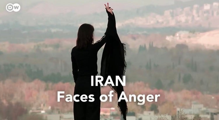 영화 〈Inside the ‘Woman, Life, Freedom’ protest movement in Iran〉 속 장면, 검은색 옷을 입은 여성이 한 손을 올리고 있는 뒷모습 (출처: DW Documentary 