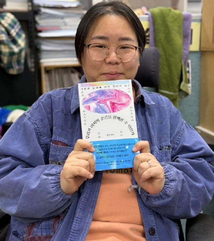 캔디 작가가 책 『우리가 마지막 순간을 함께할 수 있을까? - 사랑과 돌봄에 관한 퀴어한 참조』를 들고 웃고 있다. (제공: 캔디)    