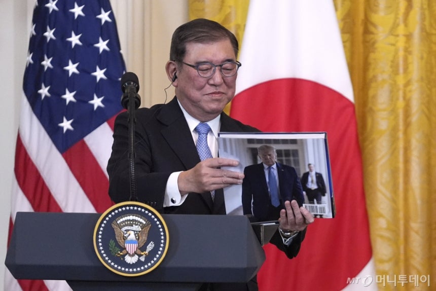 [워싱턴=AP/뉴시스] 이시바 시게루 일본 총리가 7일(현지 시간) 미국 백악관에서 열린 정상회담 후 공동 기자회견에서 도널드 트럼프 미국 대통령이 선물한 책을 들여다보고 있다. 2025.02.08. /사진=권성근