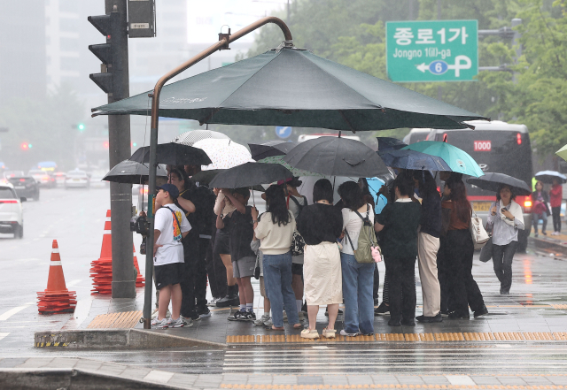5월 26일 오후 비가 내리는 서울 광화문광장에서 시민들이 파라솔 아래 우산을 쓴 채 보행신호를 기다리고 있다. 연합뉴스