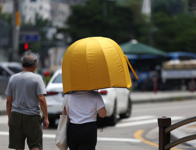 불볕더위가 이어진 지난 21일 오후 서울시내에서 한 시민이 햇빛을 가리기 위해 우산을 쓰고 이동하고 있다. 연합뉴스