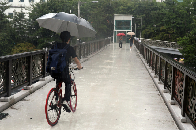 대전 서구 도심에서 갑자기 장맛비가 거세지자 한 시민이 우산을 펼쳐 들고 자전거를 타고 있다. 연합뉴스