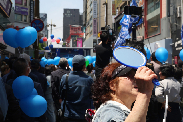이재명 더불어민주당 대선 후보가 14일 부산 부산진구 서면거리에서 유권자들에게 지지를 호소하고 있는 가운데 지지자가 저격수의 시야를 방해하기 위해 거울로 주변 건물을 향해 빛을 반사시키고 있다. 부산=오승현 기자 2
