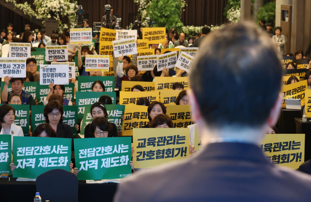 박민수 보건복지부 2차관이 21일 서울 용산구 피스앤파크컨벤션에서 열린 간호법 제정에 따른 진료지원업무 제도화 방안 공청회에서 인사말을 하는 동안 대한간호협회 회원들과 공공운수노조 의료연대본부 조합원들이 항의 피켓을
