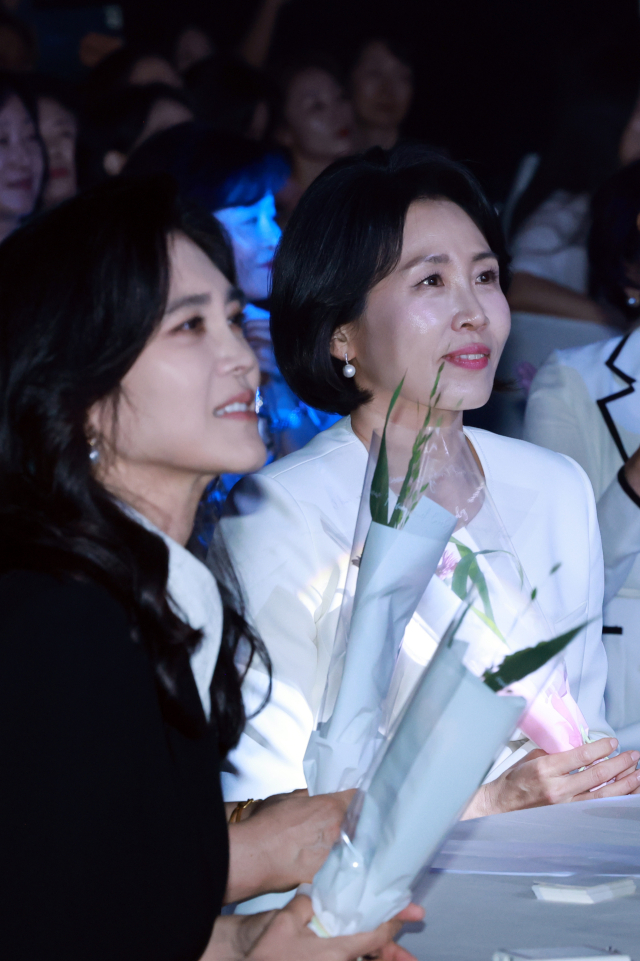 이재명 대통령의 배우자 김혜경 여사가 1일 서울 중구 신라호텔 다이너스티홀에서 열린 제4회 여성기업주간 개막식에 참석해 어린이 합창단원에게 받은 꽃을 들고 축하 공연을 보고 있다. 왼쪽은 이부진 호텔신라 사장. 연합