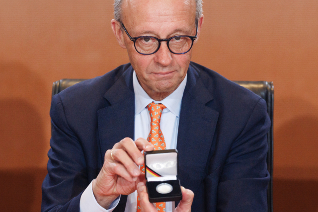 프리드리히 메르츠 독일 총리가 14일(현지 시간) 베를린에서 열린 각료회의에서 과거 서독 초대 총리인 콘라트 안데나워 탄생 150주년을 맞아 제작된 기념 주화를 들어 보이고 있다.EPA연합뉴스