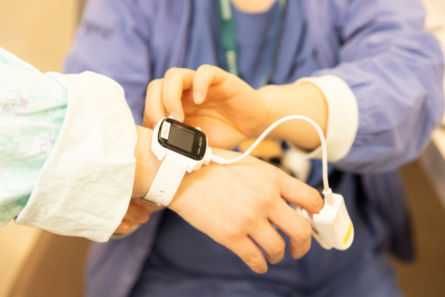 이대서울병원 순환기내과 병동 간호사가 환자에게 스마트 병상 모니터링 시스템‘씽크’의 웨어러블 기기를 끼워주고 있다.사진 제공=대웅제약