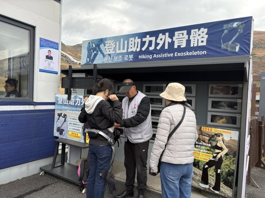 지난 25일 중국 지린성 백두산 천지로 향하는 계단 아래 외골격 웨어러블 로봇 대여소에서 관광객들이 제품을 착용하고 있다. 한 번 대여료는 98위안으로 허리와 양쪽 허벅지에 장치를 착용하면 센서가 보행을 감지해 오르