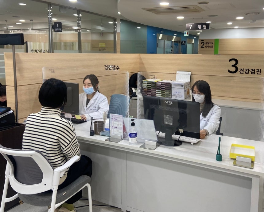 밝은 실내에서 한 여성이 건강검진 접수를 하고 있는 사진이다.두 명의 의료진이 마스크를 착용한 채 컴퓨터를 응시하며 업무를 보고 있다. [연합]