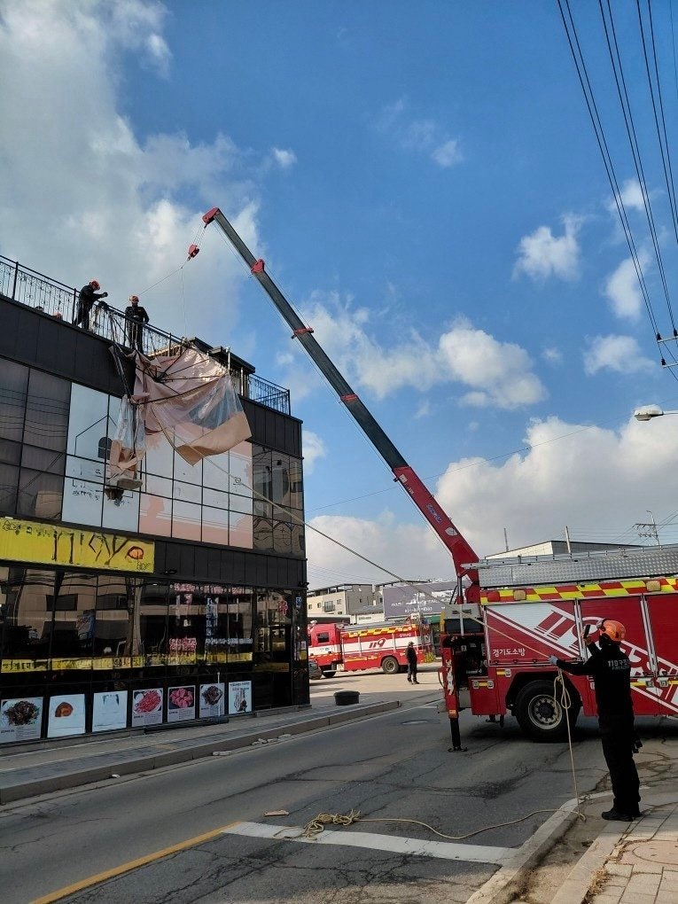 경기 고양시 일산 옥상에 설치되어 있는 캐노피 천막 구조물이 강풍으로 탈락돼 소방 당국이 크레인을 활용해 지상으로 인양 작업을 벌이고 있다.(경기소방재난본부 제공) 뉴스1