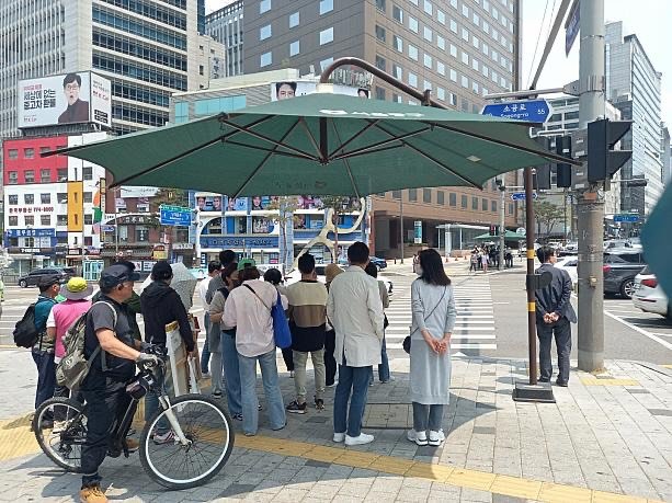 횡단보도를 건너려는 시민들이 그늘막 아래 모여 신호를 기다리고 있다. 사진=스레드 갈무리 