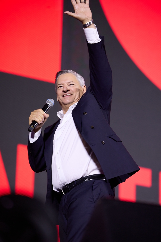 Netflix共同CEOのテッド・サランドス氏がステージで手を挙げ、マイクを持つ