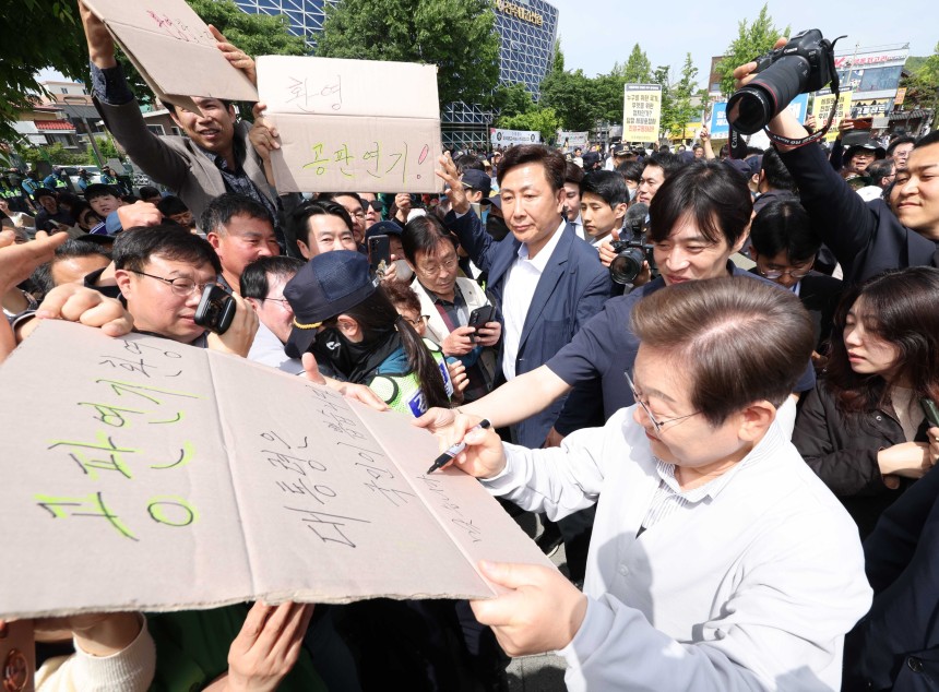 이재명 더불어민주당 대선후보가 7일 전북 전주시 완산구 풍남문 인근에서 공판연기를 환영하는 지지자의 응원 피켓에 사인을 해주고 있다.'공판연기 환영,대통령은 국민이 뽑습니다'라고 적힌 피켓에 이 후보는 '맞습니다