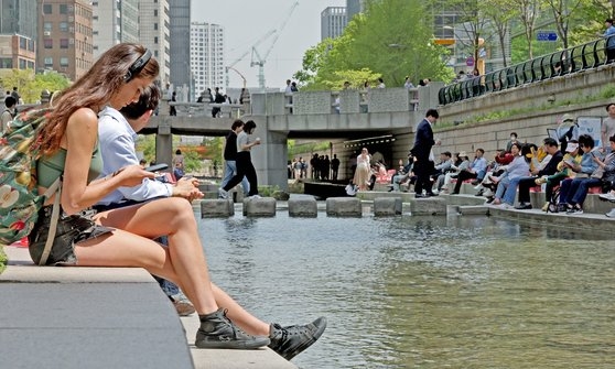 서울지역 낮 최고기온이 25도까지 오르며 초여름 날씨를 보인 18일 오후 서울 중구 청계천을 찾은 관광객이 물가에 앉아 더위를 식히고 있다. 뉴스1
