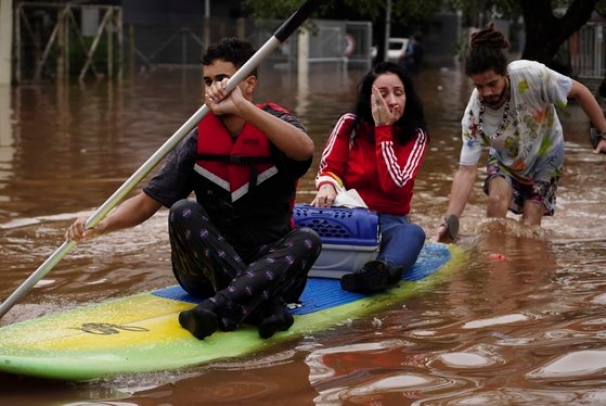 4일(현지시간) 브라질 리오그란지두술주 카노아스에서 폭우로 물에 잠긴 동네에서 사람들이 서핑보드를 타고 대피하고 있다.AP=연합뉴스