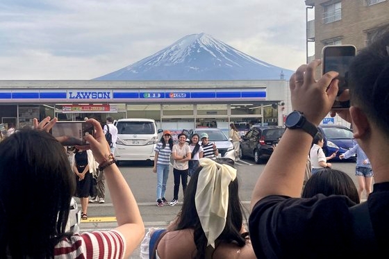 관광객들이 지난달 28일 일본 야마나시현 후지카와구치코 마을의 한 편의점 앞에서 후지산을 배경으로 한 사진을 찍고 있다. AP=연합뉴스