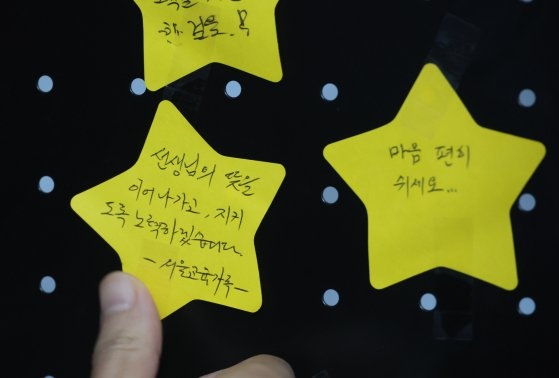 서이초 교사 사망 1주기를 하루 앞둔 17일 오전 종로구 서울시교육청에 마련된 추모 공간을 찾은 한 시민이 추모 메시지를 붙이고 있다. 연합뉴스