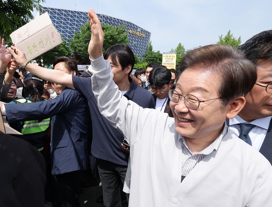 더불어민주당 이재명 대선 후보가 '골목골목 경청투어:국토종주편'에 나선 7일 전북 전주시 풍남문 앞 광장에서 지지자가 든 공판 연기 환영 팻말을 지나고 있다. 연합뉴스