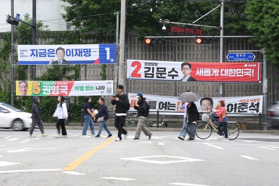 15일 경기도 의정부시의 한 교차로에서 길을 건너는 시민들 뒤로 제21대 대통령 선거 후보들의 현수막이 걸려 있다. 연합뉴스