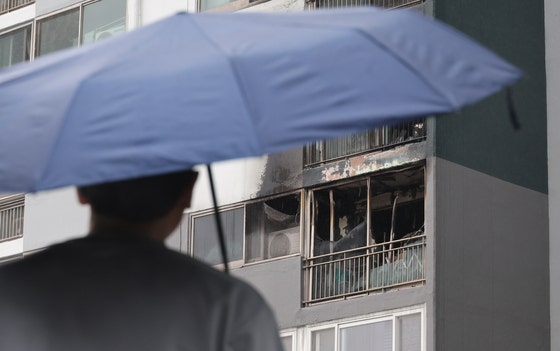 지난 24일 오전 어린이 2명이 숨진 부산진구의 한 아파트 화재 현장에서 한 시민이 우산을 쓰고 지나고 있다. 이날 오전 4시 15분께 한 아파트 4층에서 부모가 일을 나간 사이 불이 나 10살 언니와 7살 동생이 