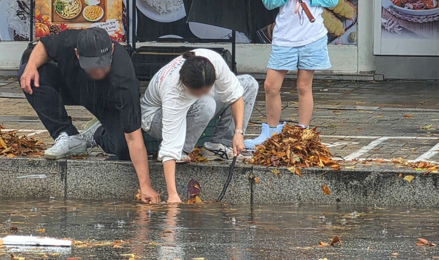 폭우가 쏟아진 18일 경기도 고양시 일산서구에서 시민들이 낙엽이 배수구를 막아 도로가 물바다가 되자 손으로 낙엽을 걷어내고 있다. 연합뉴스