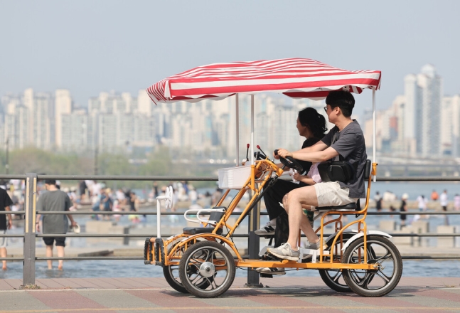 차양이 달린 다인승 자전거를 탄 시민들이 물놀이하는 이들을 바라보고 있다. 김영원 기자