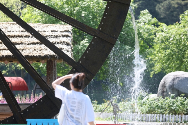 지난 3일 오후 대구 달성군 송해공원을 찾은 시민이 햇빛을 손으로 가리며 물레방아 앞을 지나가고 있다. 연합뉴스