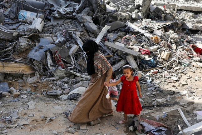 9일(현지시각) 팔레스타인 가자 중부 누세이라트 남민 캠프에서 한 여성과 어린이가 이스라엘 공격으로 무너진 건물 잔해 사이로 걸어가고 있다. 로이터 연합뉴스