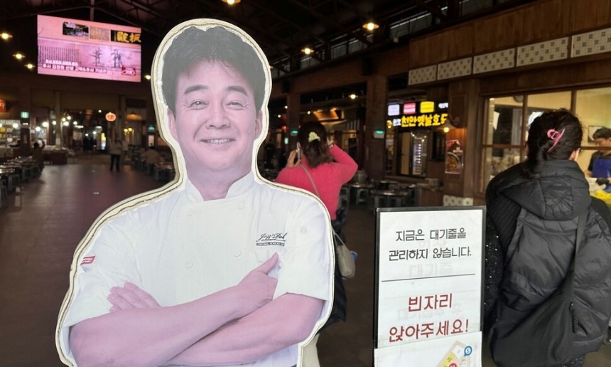 지난 10일 오후 충남 예산상설시장 광장 입구에 세워진 백종원 더본코리아 대표의 사진 입간판 옆으로 방문객들이 들어서고 있다.송인걸 기자