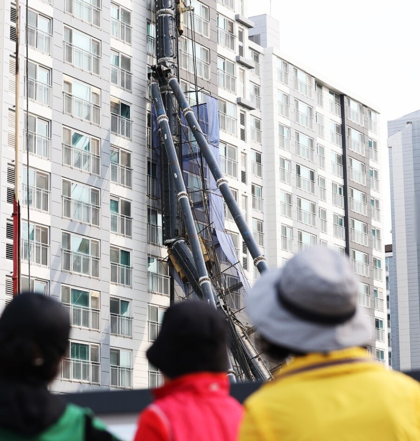 시민들이 6일 경기도 용인시 기흥구 서천동 인덕원∼동탄 복선전철 공사 현장에서 천공기가 넘어져 인근 아파트 건물 벽면에 기댄 채 쓰러져 있는 모습을 바라보고 있다. 해당 천공기는 5일 밤 10시13분께 전도해 아파트
