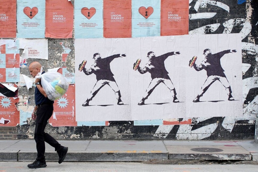 21일(현지시각) 워싱턴 시내 거리에서 거리 예술가인 뱅크시의 스타일을 패러디해, 샌드위치를 던지는 남성을 그린 포스터 앞으로 한 시민이 지나가고 있다. 길쭉한 샌드위치 빵(저항의 표시로 샌드위치를 ​&#