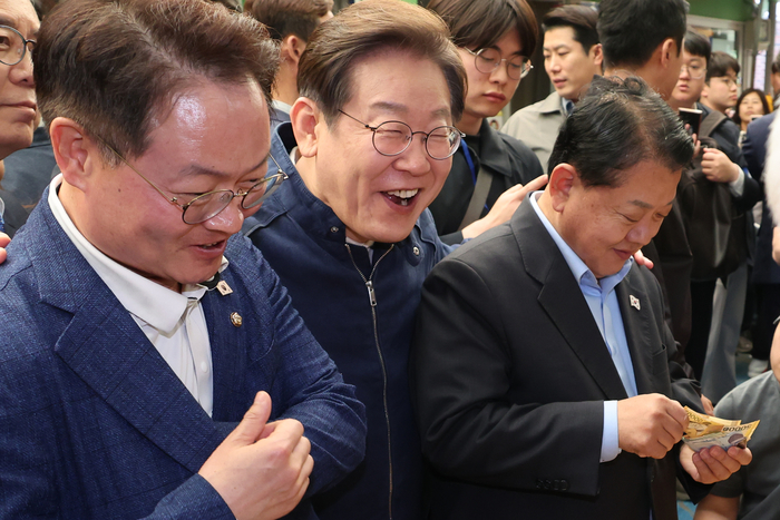 더불어민주당 이재명 대선 후보가 '골목골목 경청투어' 접경지역 방문 이틀째인 2일 강원도 인제군 원통전통시장에서 건어물 가게에 들러 황태채를 맛본 뒤 김병주(오른쪽)·허영 의원에게 구입을 권하고 있다.연합뉴스