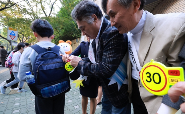 서울 양천구 양명초등학교 앞에서 등교하는 학생에게 ‘어린이보호구역 시속 30km 이하 운행’을 홍보하는 가방 고리를 달아주고 있다. 연합뉴스