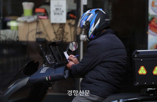 2021년 11월 서울 중구의 한 거리에서 한 배달 노동자가 잠시 멈춰 서서 종이에 무언가 쓰고 있다. 한수빈 기자